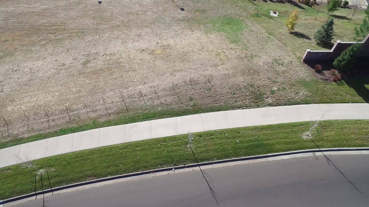 Aerial view of sidewalk, road, lawn, and a walled property corner