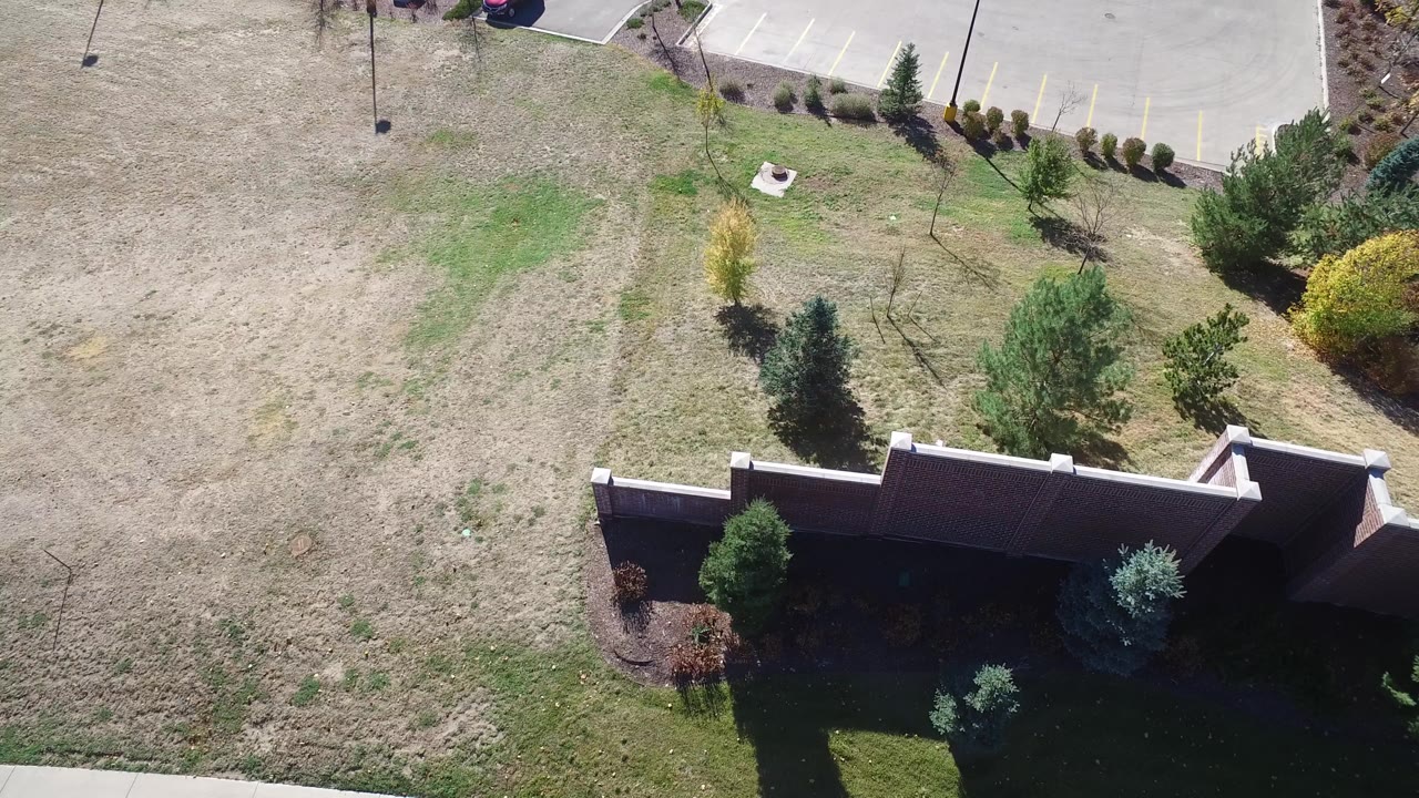 Overhead view of grass, trees, a wall, and the edge of a parking lot.