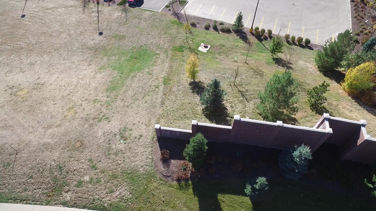 Aerial view in Hidden Lake, Colorado with a masonry-style wall crossing the lower frame, small trees and shrubs in the grass, parking spaces above, and no visible people.