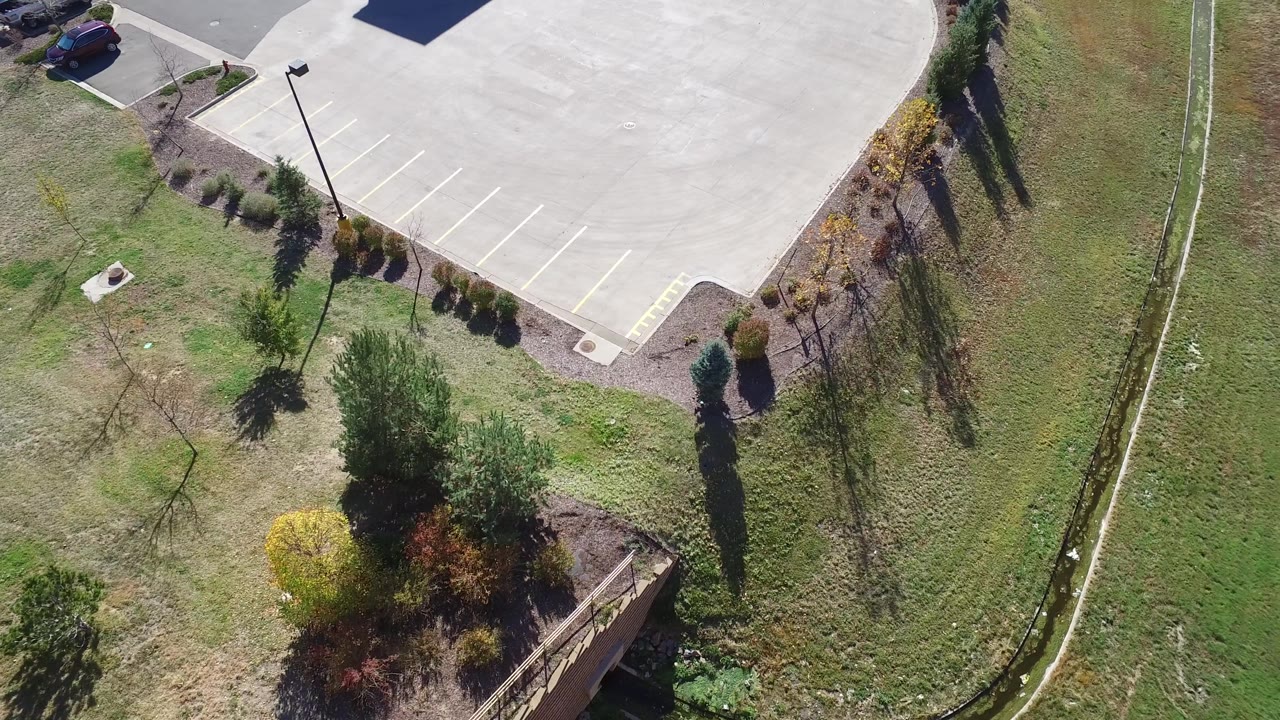 Top-down frame of pavement, planted shrubs, grass, trees, and a drainage ditch.