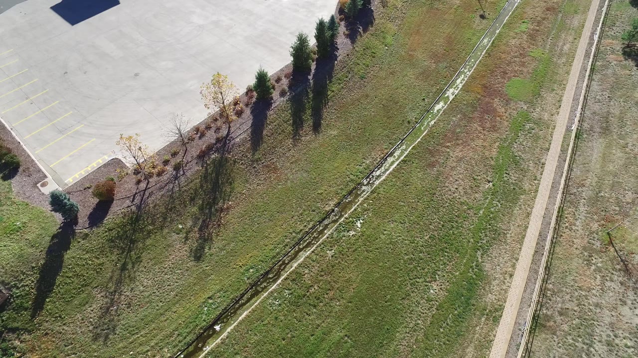 Aerial frame in Hidden Lake, Colorado with green and dry grass patches, a narrow channel through the middle, parking pavement at upper left, and no visible people.