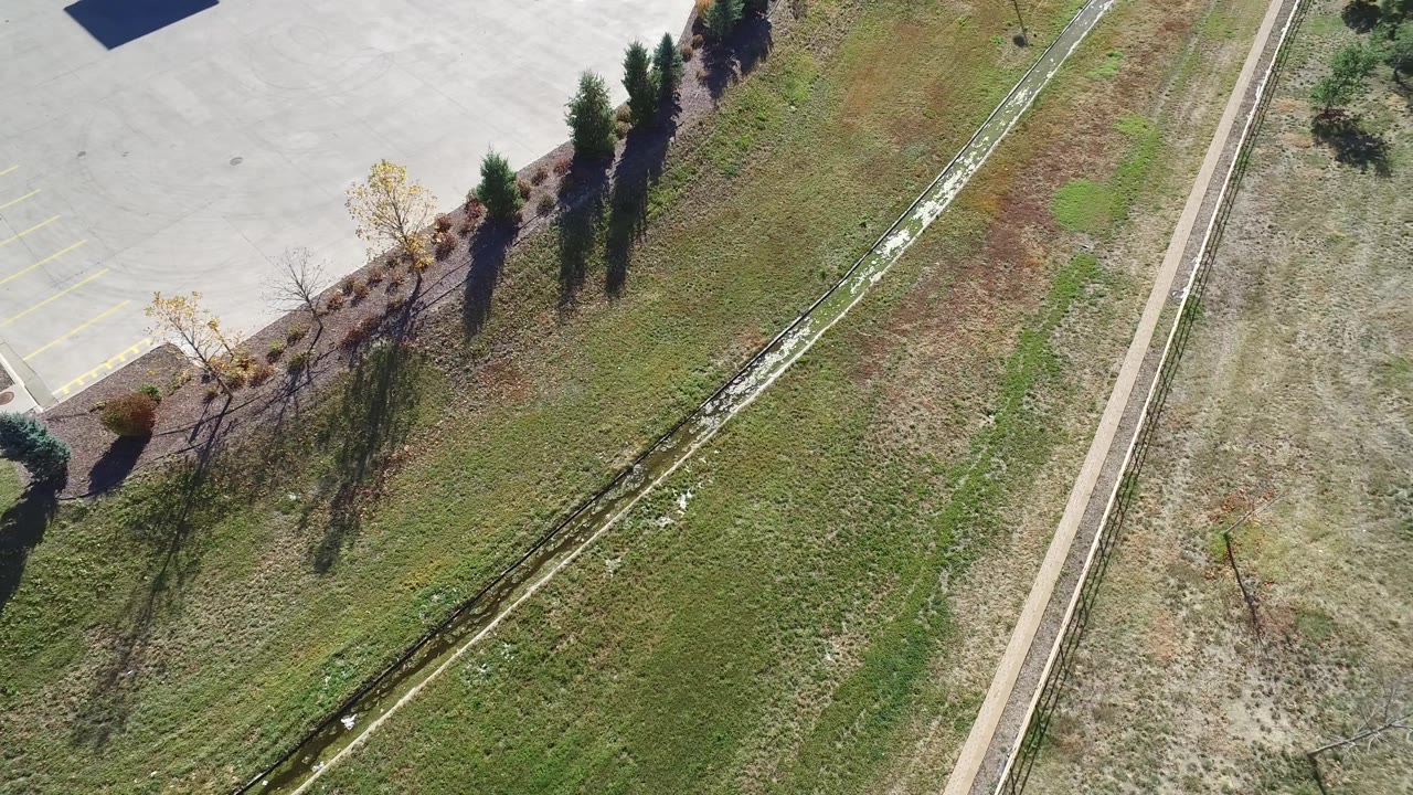 Overhead suburban grass area with trees, channel, and road edge