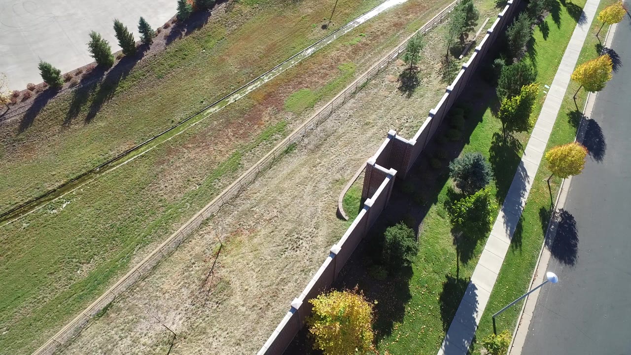 Aerial view of a road, sidewalk, brick wall, trees, and open grassland.