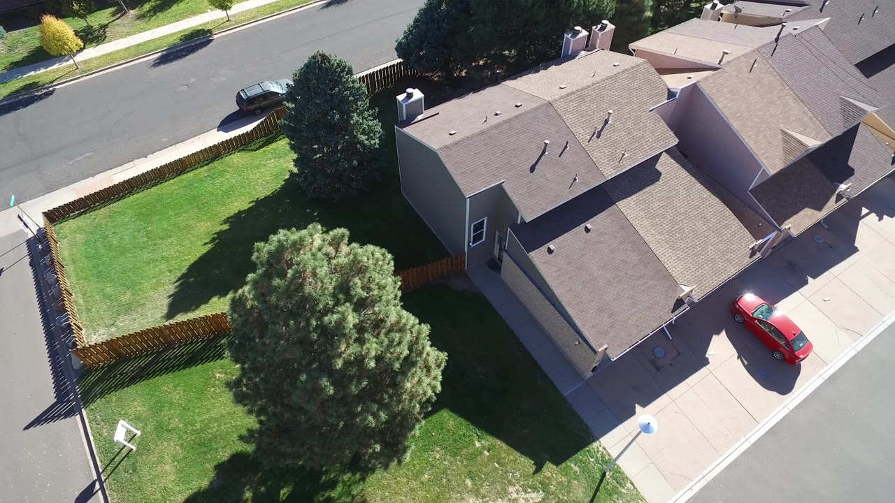 Aerial view of suburban houses, lawns, street, and a red car in a driveway.