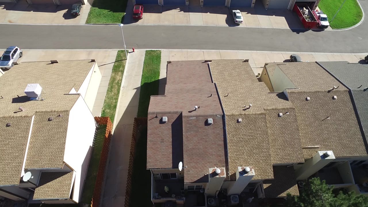 Drone view over clustered rooftops with street and parked vehicles above.