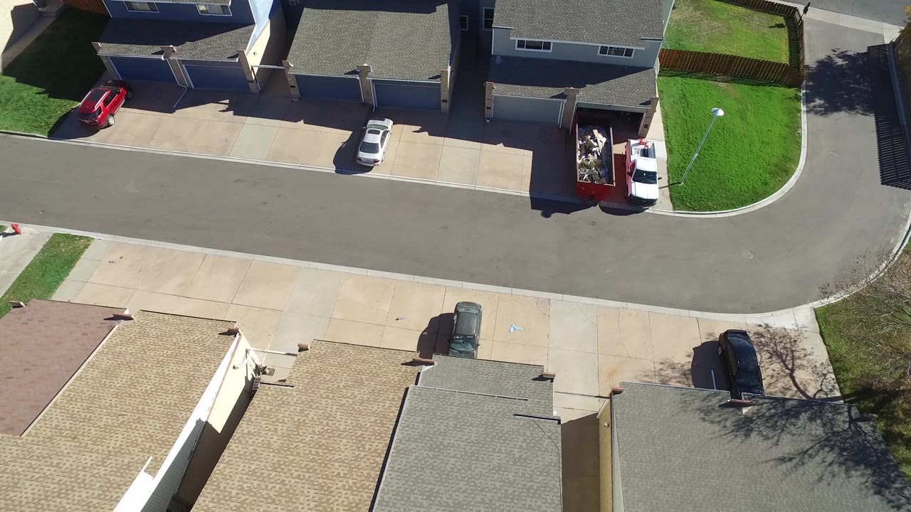 Overhead view of a curved suburban street with houses, lawns, and parked cars.