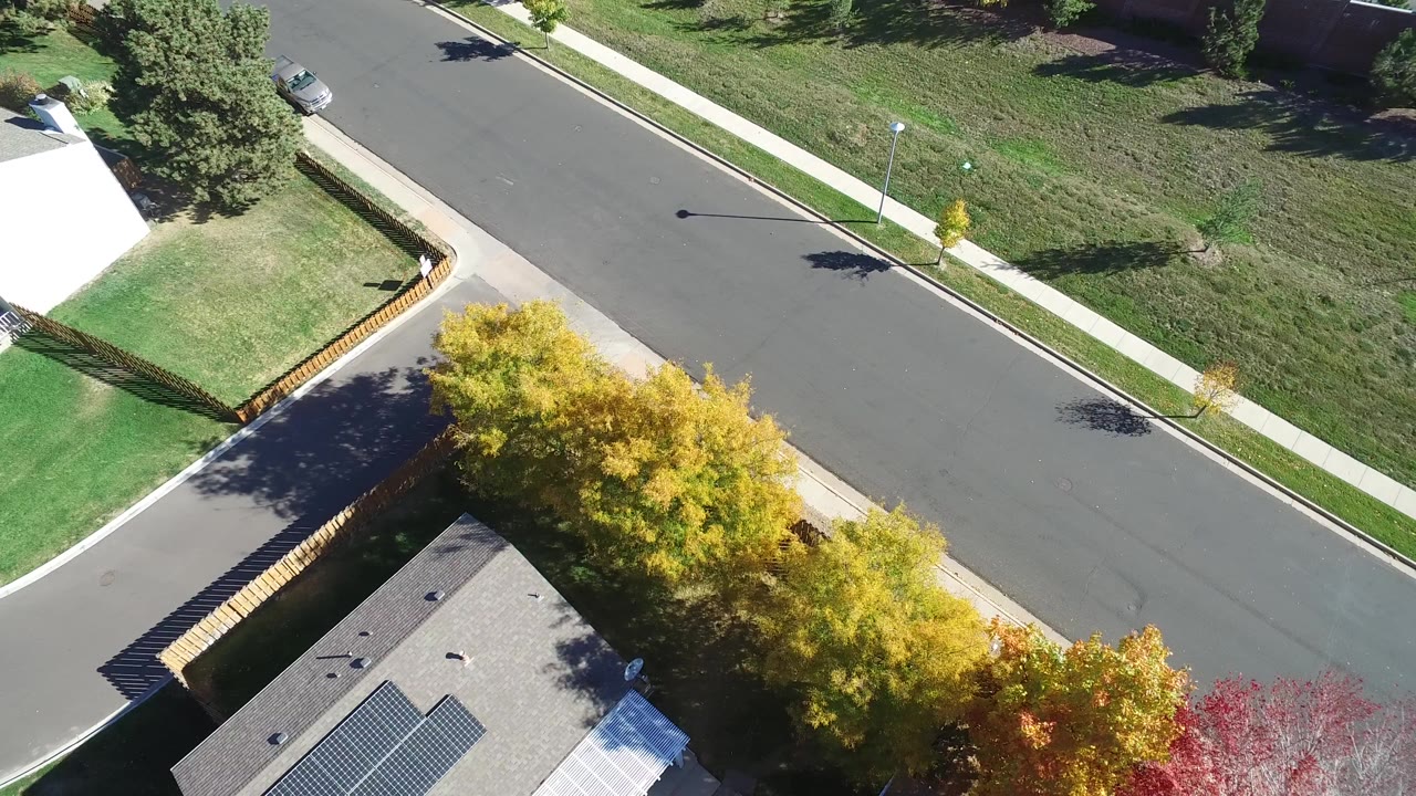 Overhead suburban road with rooftops, trees, lawns, and sidewalks.