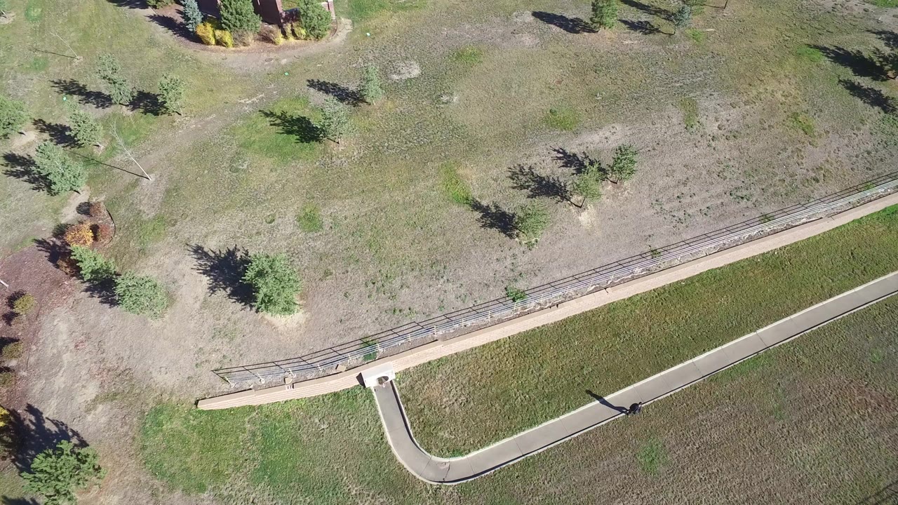 Overhead frame from Hidden Lake, Colorado showing a curved path, fenced pasture, scattered trees, dry grass, and no visible people.