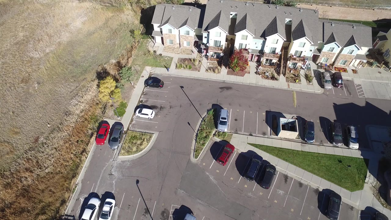 Overhead view of townhomes, parking spaces, cars, and dry open ground.