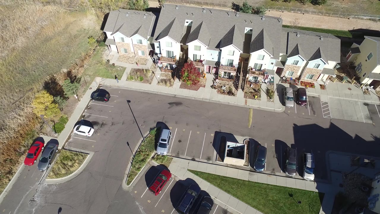 Aerial frame in Hidden Lake, Colorado showing the townhome row more centrally, with parked vehicles, marked spaces, planted beds, and no visible people.