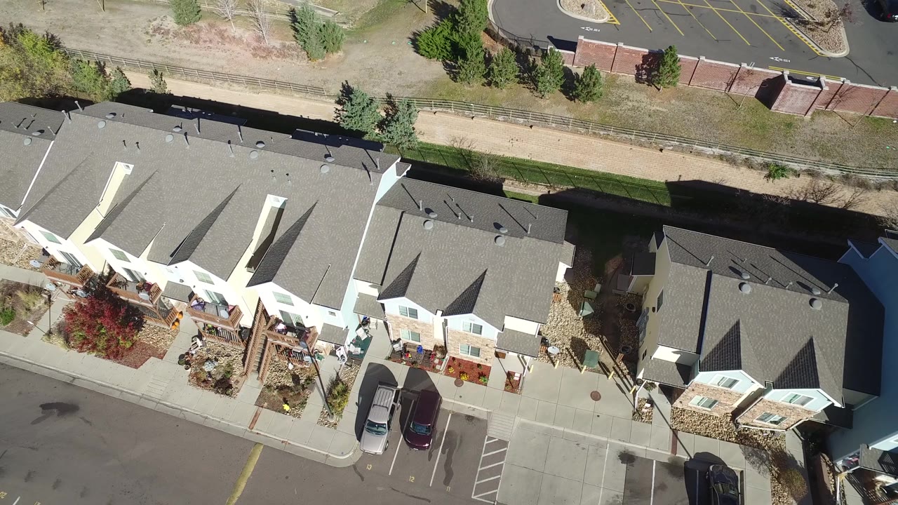 A slightly later overhead view in Hidden Lake, Colorado shows the apartment row centered below a fenced greenbelt and a parking lot, with no visible people.