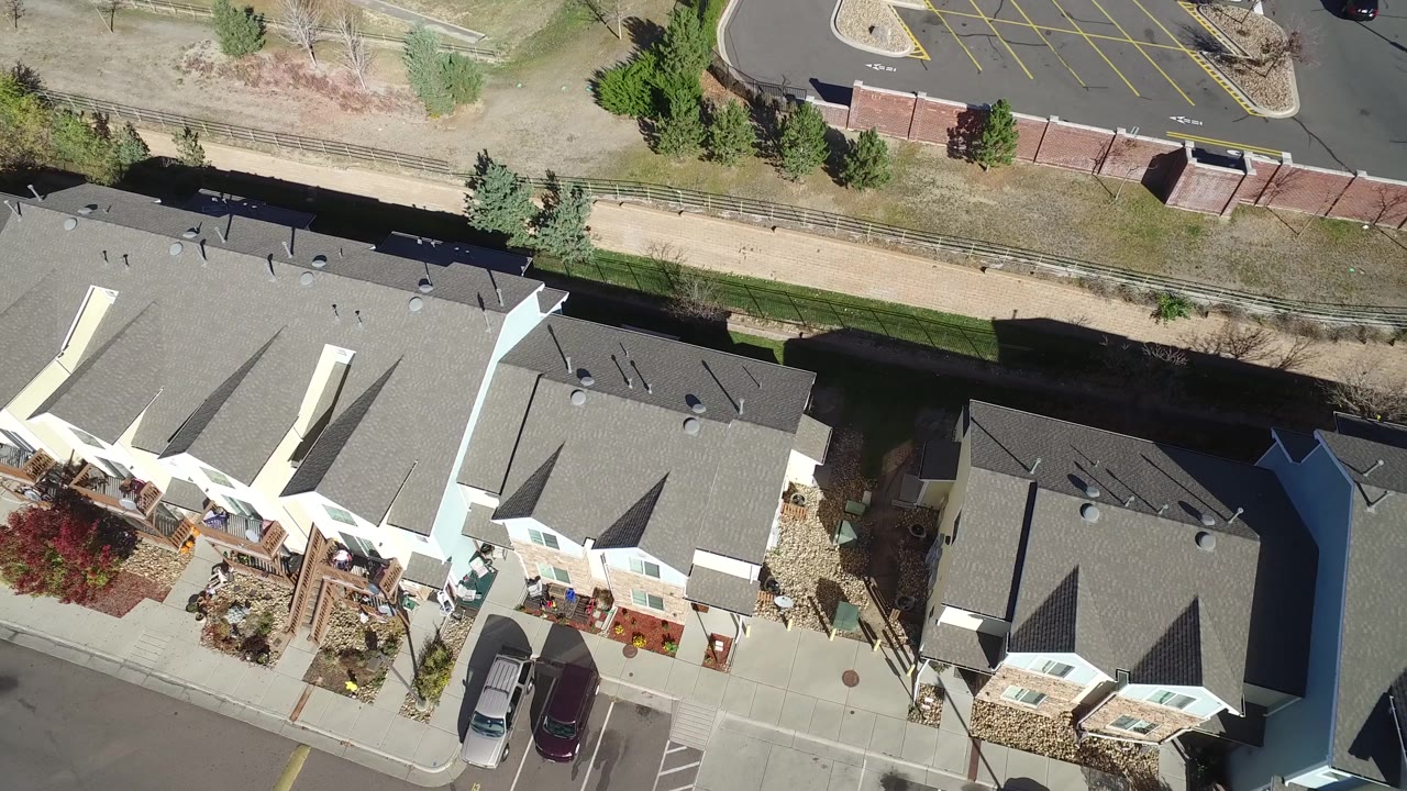 Top-down residential block with apartment roofs, cars, trees, and parking stripes.
