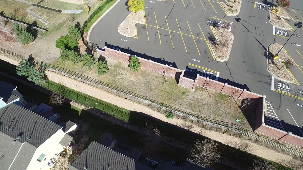 At 0:00, a high overhead view in Hidden Lake, Colorado shows an empty marked parking lot, brick wall, grassy edge, nearby rooftops, and no visible people.
