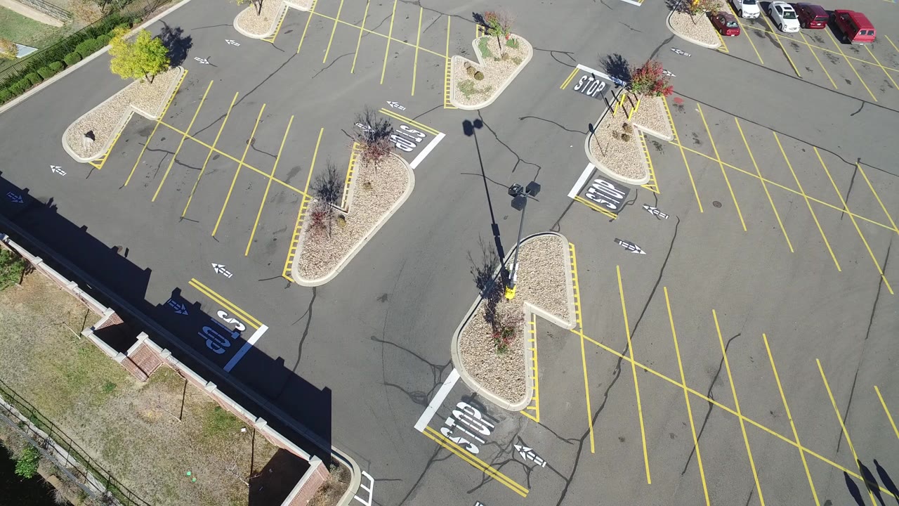 Overhead view of a mostly empty parking lot with yellow lines and landscaped islands.