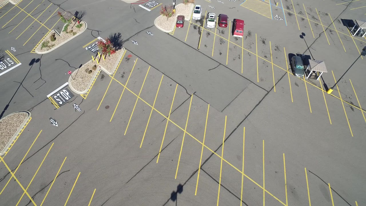 Mostly empty parking lot seen from above with a cart-return shelter and parked cars.