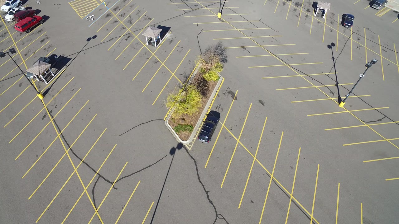 Overhead view of a mostly empty parking lot with yellow lines and a landscaped island.
