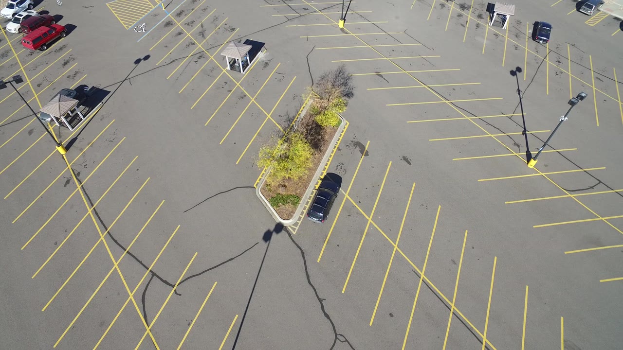 At 0:01, the drone view in Hidden Lake, Colorado centers the landscaped island below the parking rows, with long light-pole shadows crossing the asphalt and no visible people.