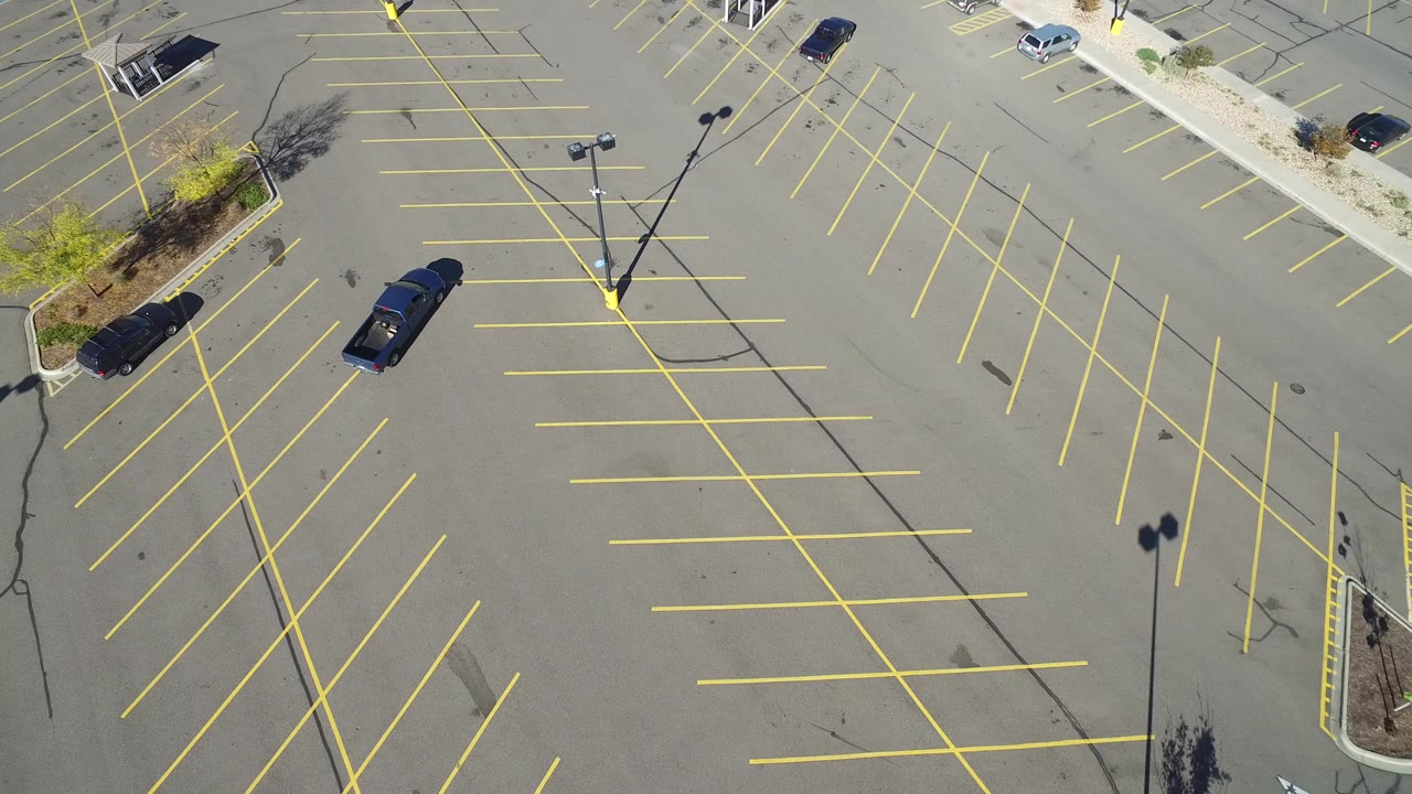 High overhead view of a mostly empty Hidden Lake, Colorado parking lot with yellow stall lines, scattered cars, planted islands, and no visible people.