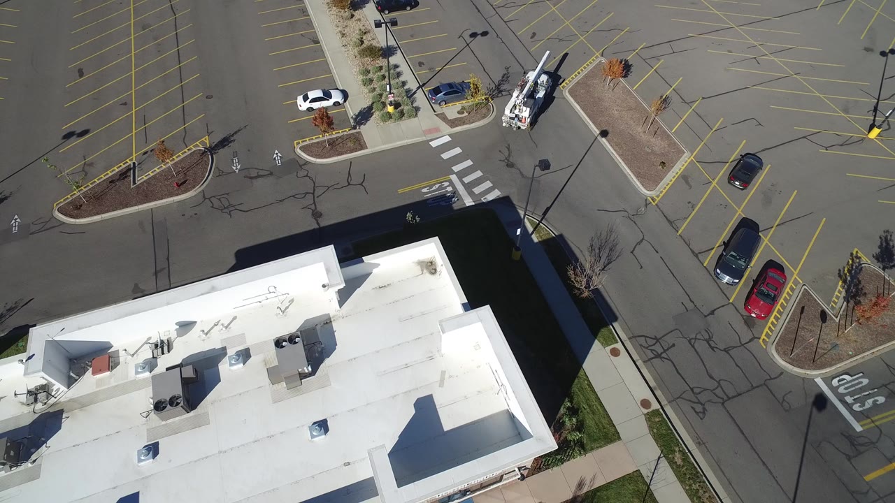 Aerial view of a white-roofed commercial building beside a mostly empty parking lot.
