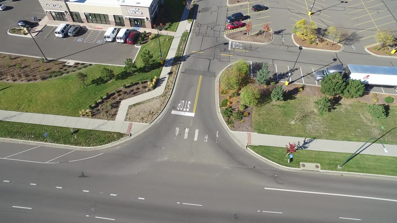 Overhead view of a road intersection beside parking lots and landscaped grass.