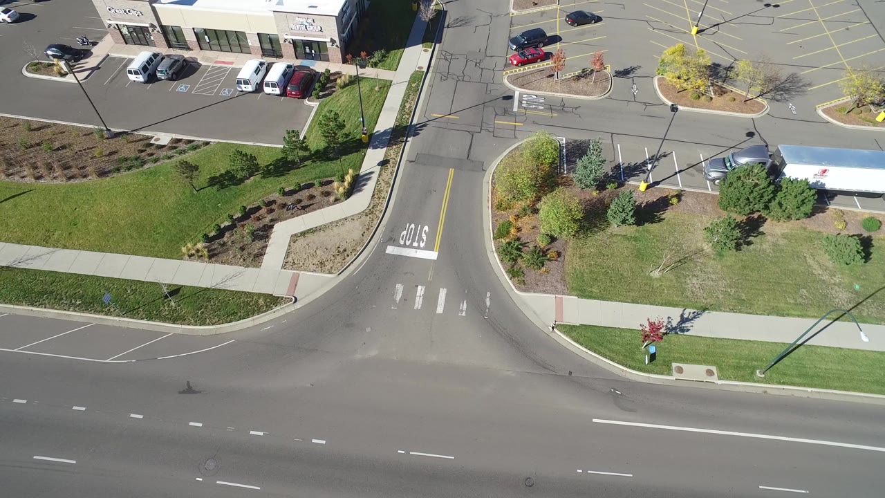 High aerial frame in Hidden Lake, Colorado with the intersection centered lower in the view, parking spaces and low commercial buildings at the top, and no visible people.