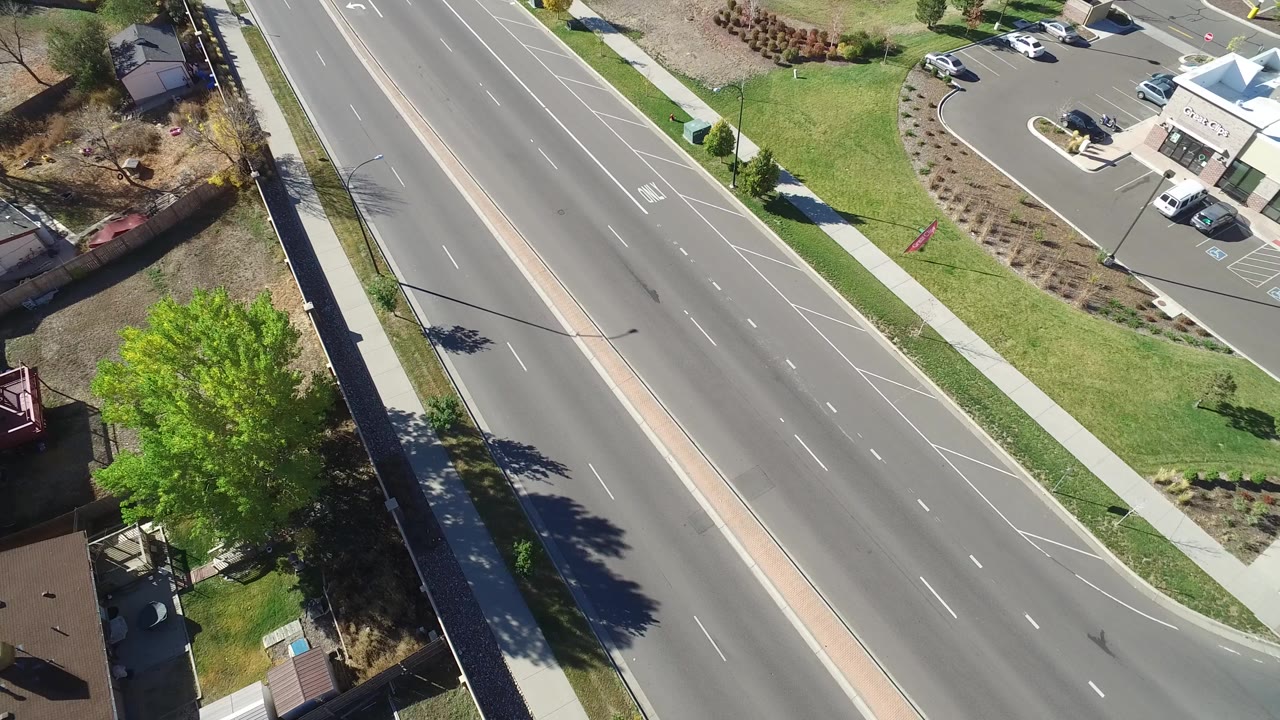 High aerial view in Hidden Lake, Colorado showing a divided multi-lane road, sidewalks, rooftops, lawns, and trees with no visible people.