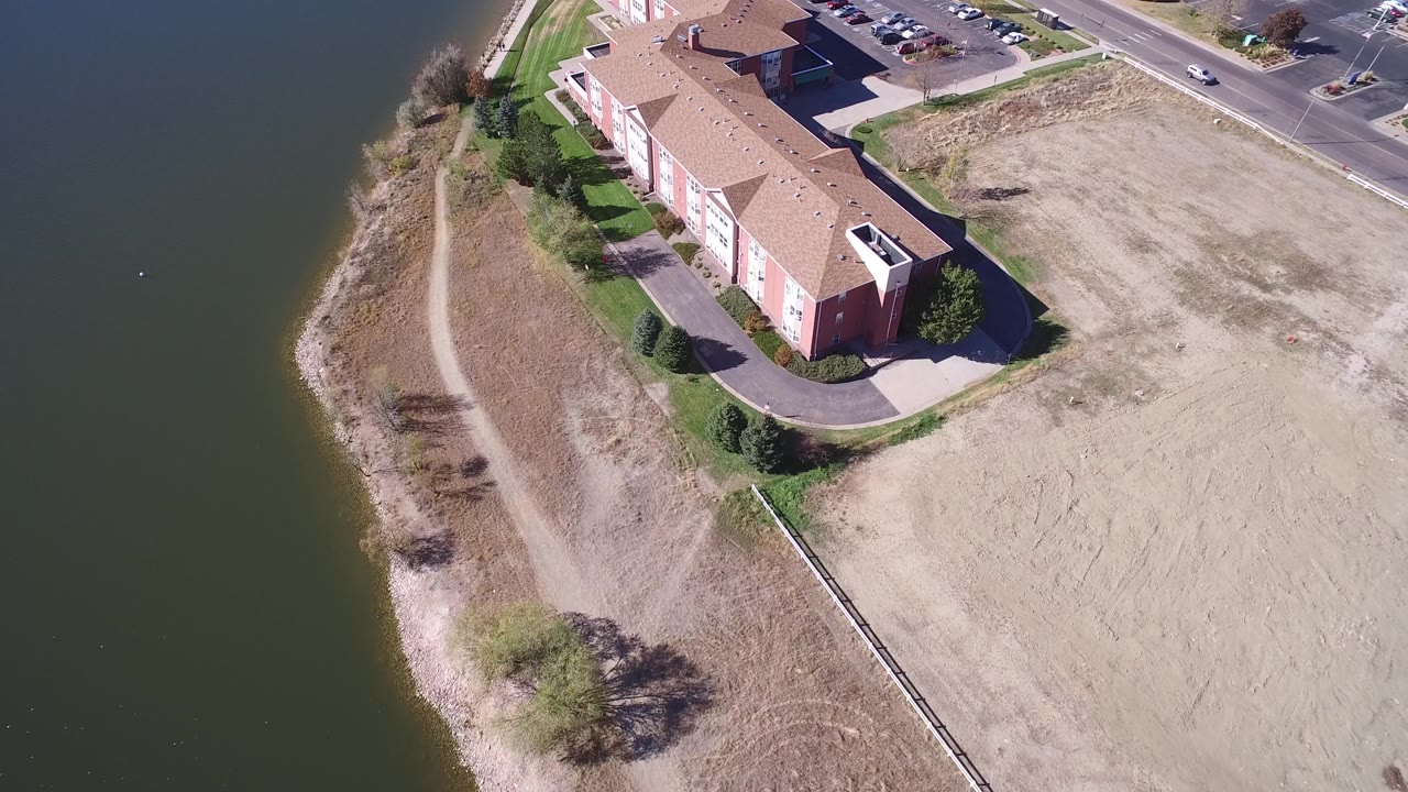 The second frame holds a slightly shifted aerial view of the Hidden Lake residential building, with the shoreline path more centered along the water and no visible people.