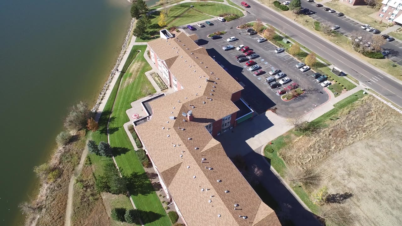 Top-down drone view of building, parking lot, road, and lake edge