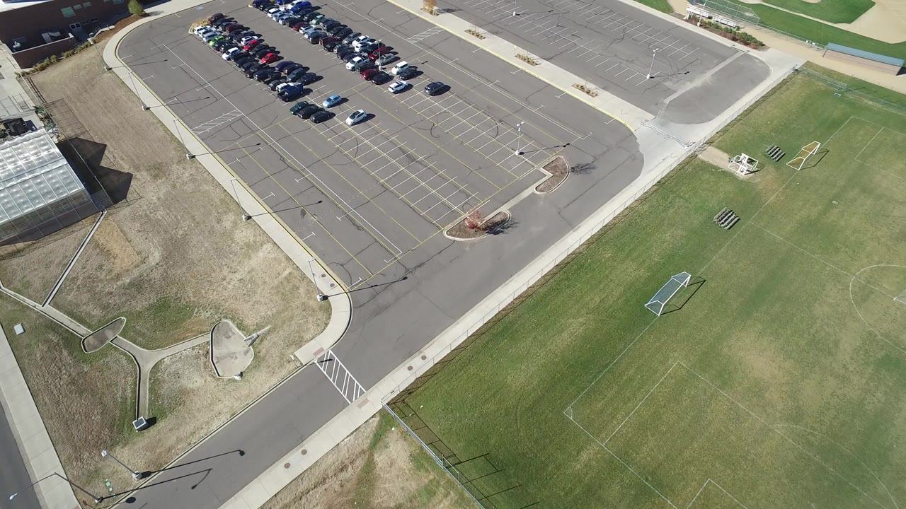 High aerial view in Hidden Lake, Colorado showing a parking lot with parked cars, empty marked spaces, sidewalks, grass fields, and no visible people.