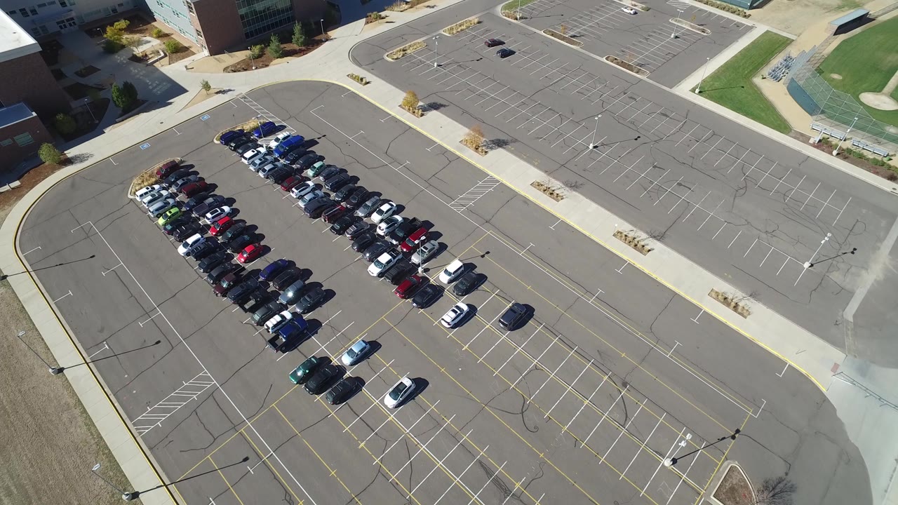 Aerial view of parked cars in a partly full asphalt parking lot.