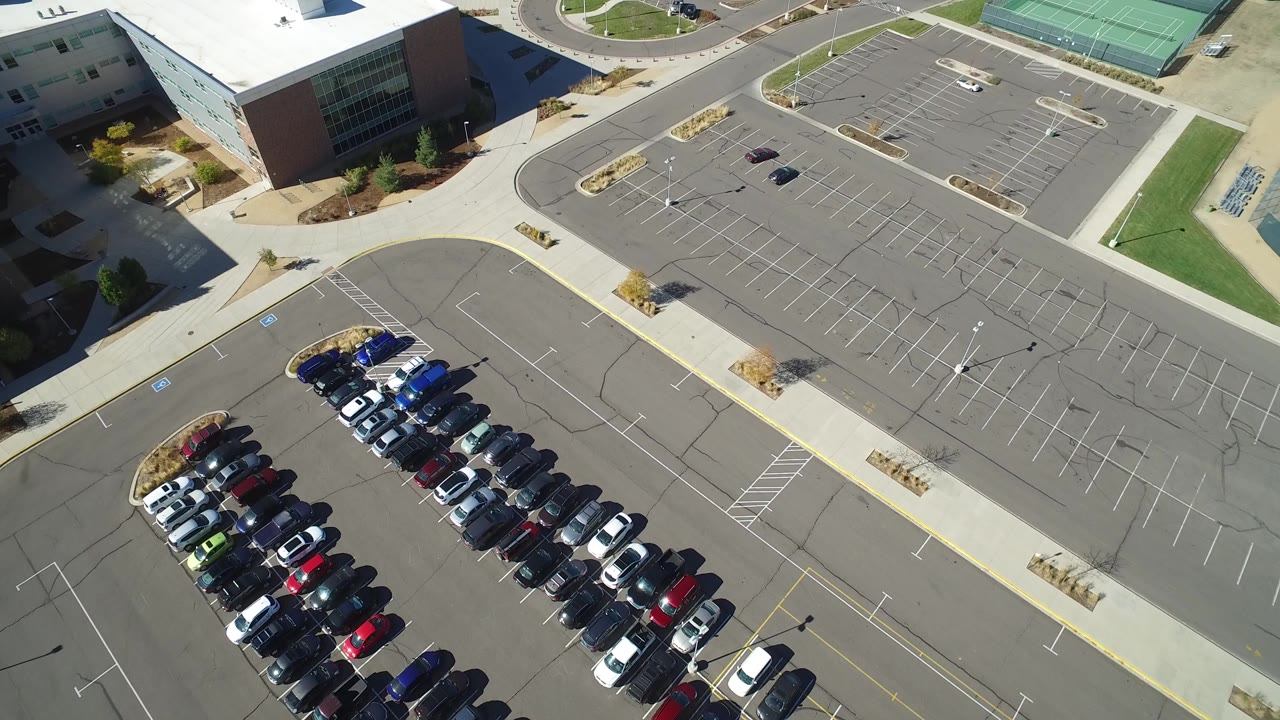 Overhead view of a commercial building parking lot with parked cars and empty spaces.