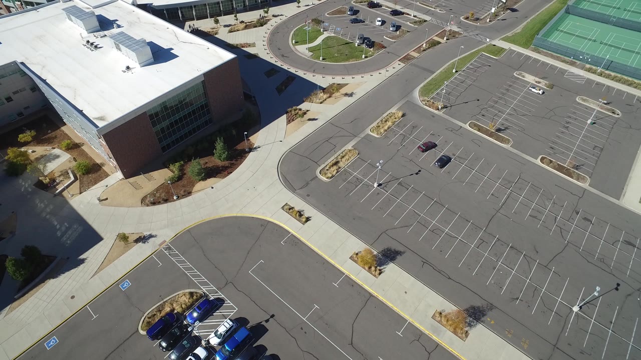 Aerial view of a large building beside an empty parking lot and tennis courts.