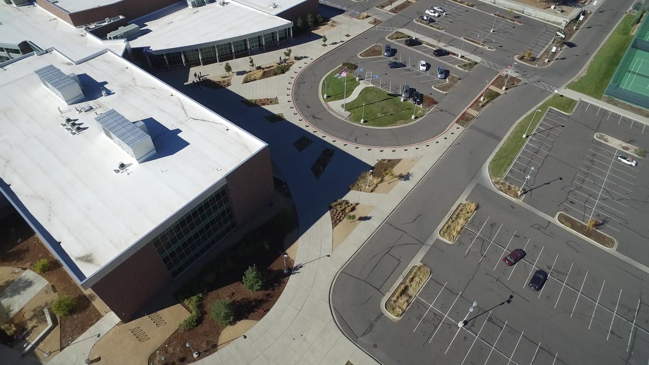 Second aerial frame in Hidden Lake, Colorado showing the office complex roofline, circular drive area, parking stalls, scattered cars, and no visible people.