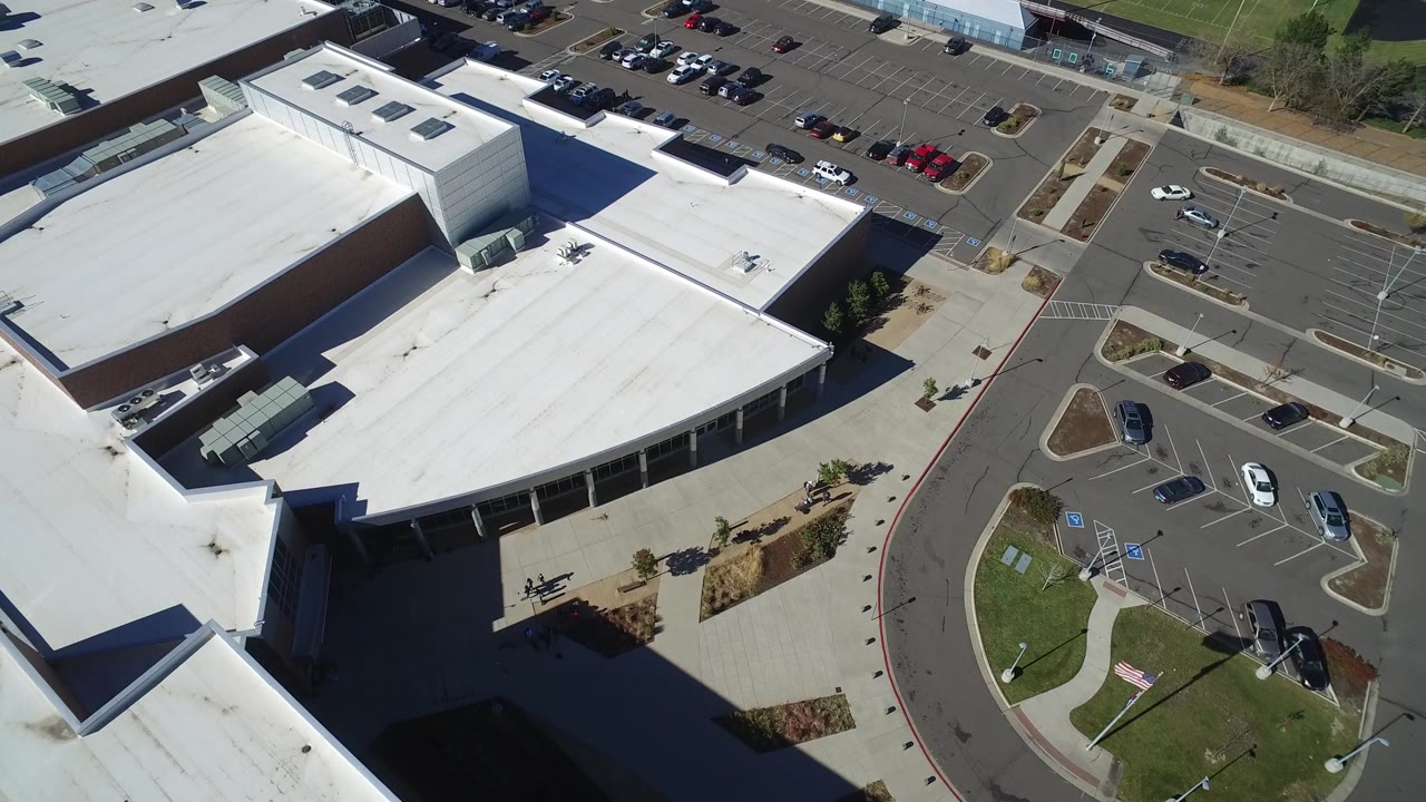 High aerial frame in Hidden Lake, Colorado with the main white roof centered, small cars spread across marked stalls, sidewalks, grass, and no visible people.