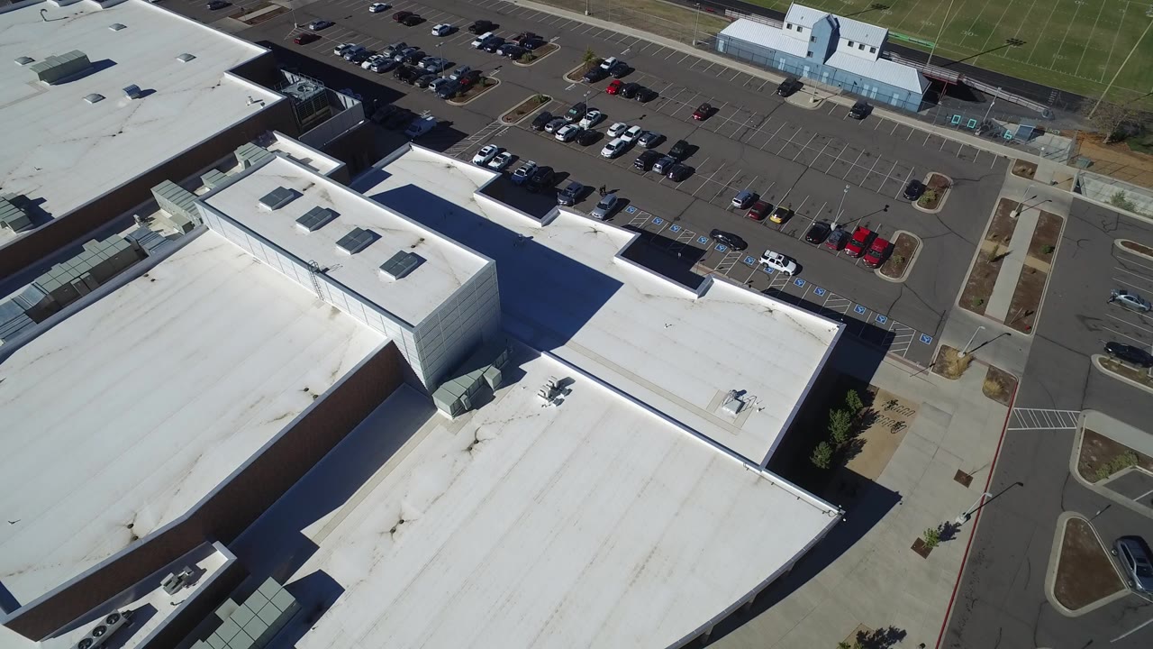 Aerial view of white rooftops beside a parking lot with parked cars.