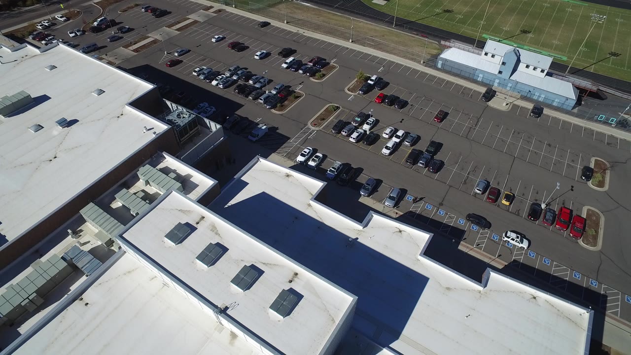 Aerial view of a white-roofed building, parking lot, road, and sports fields.