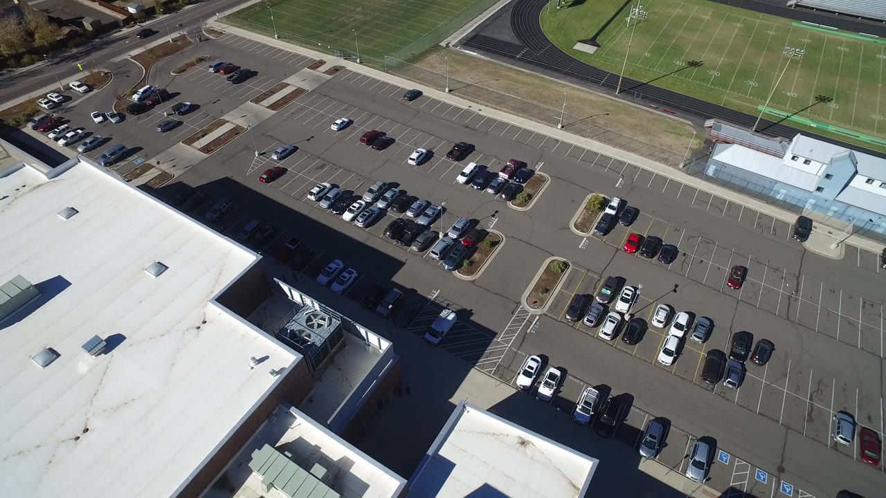 Aerial view of a commercial parking lot beside a white-roofed building and sports field.
