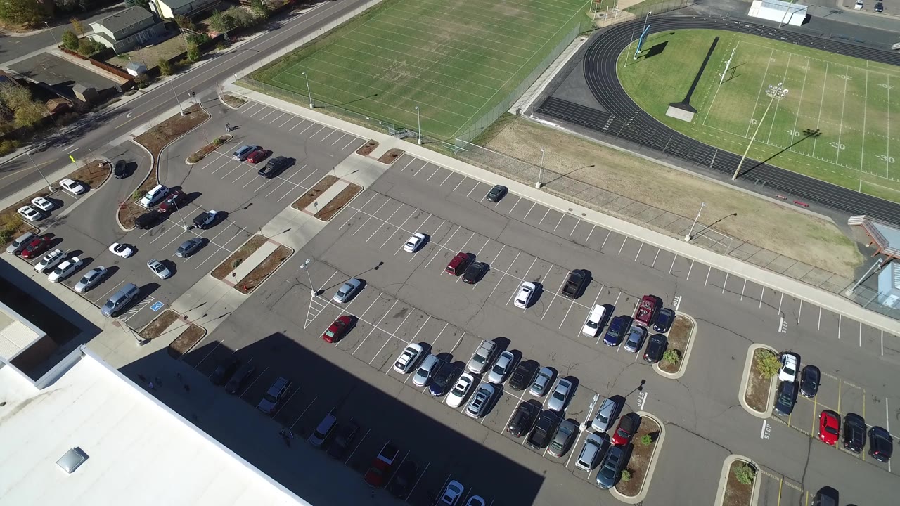 Top-down view of a school-like parking area next to a sports field.