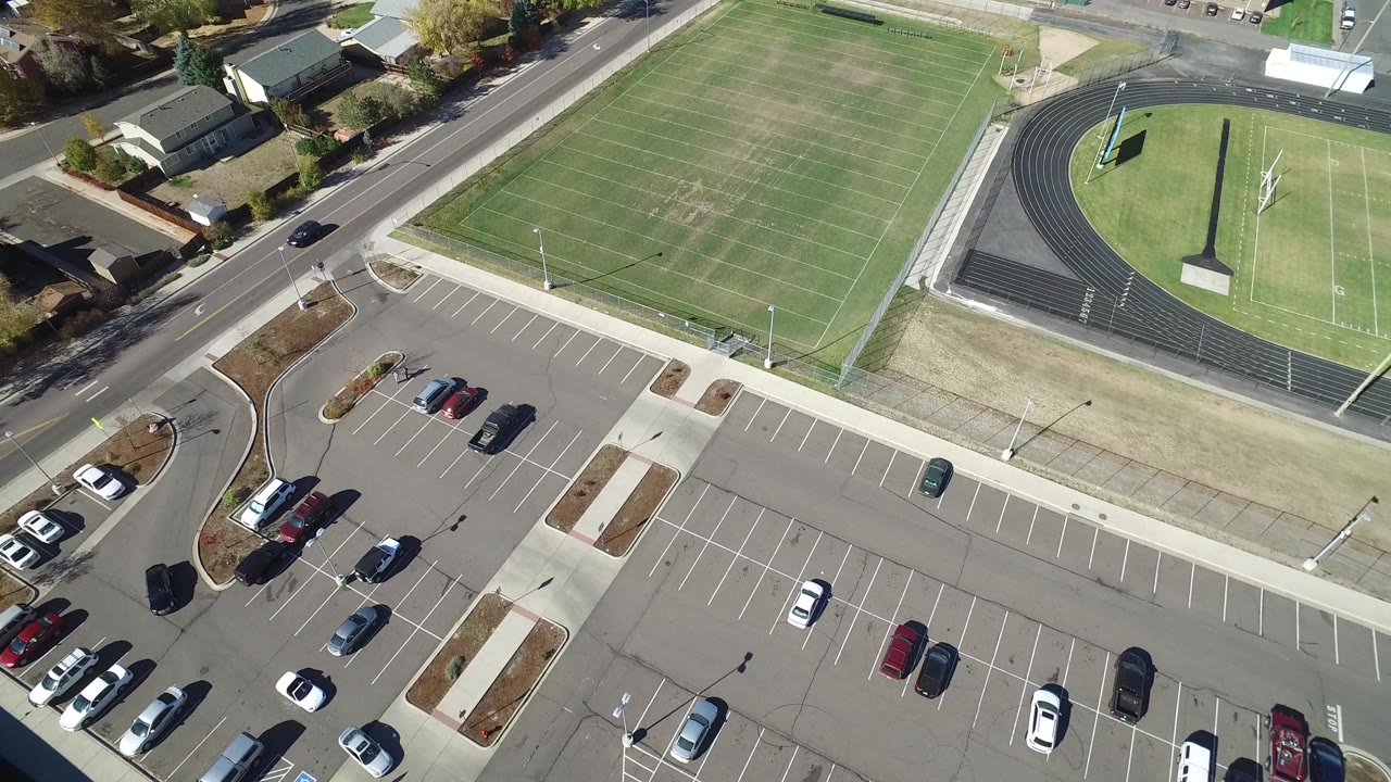 Drone-style overhead of field, track, road, and parking rows.