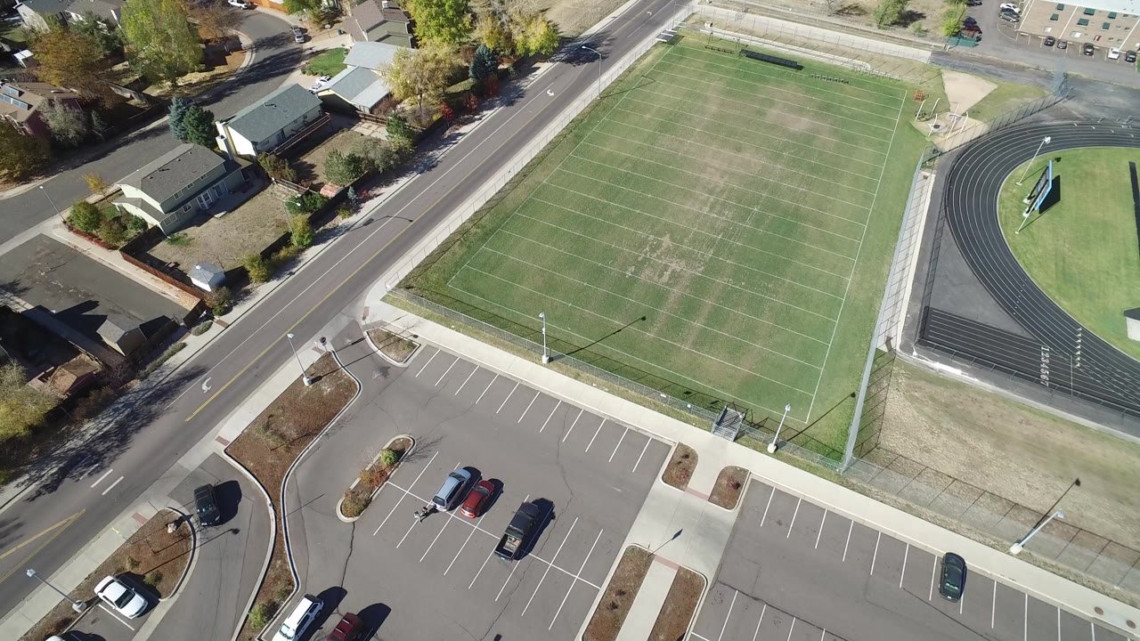 Opening aerial frame over Hidden Lake, Colorado shows a lined football field, curved running track, road, houses, and parking lot with no visible people.