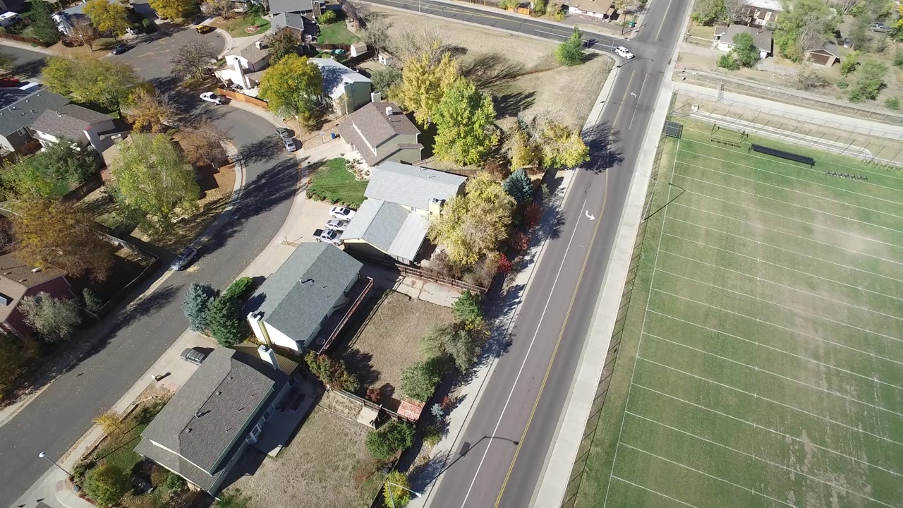 Overhead drone view of houses, streets, and a green sports field.