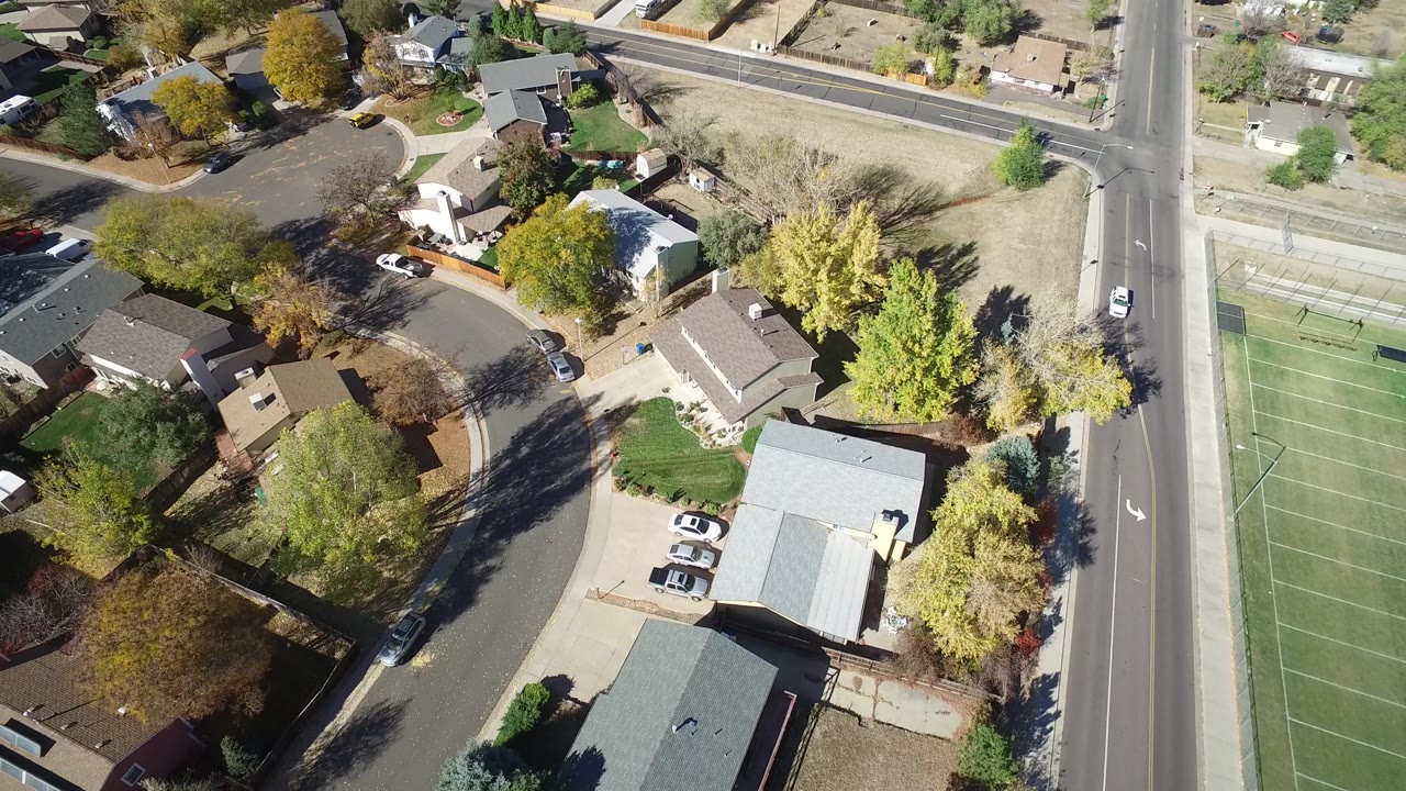 At 0:01, the aerial view over Hidden Lake, Colorado includes a green tennis court on the left, residential roofs, driveways, trees, and no visible people.