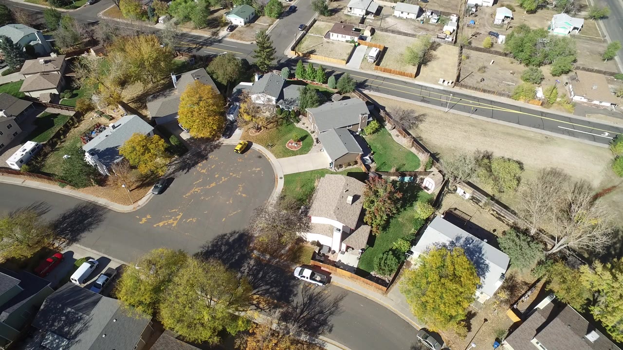 Aerial view of a curved residential street with houses, trees, lawns, and parked cars.