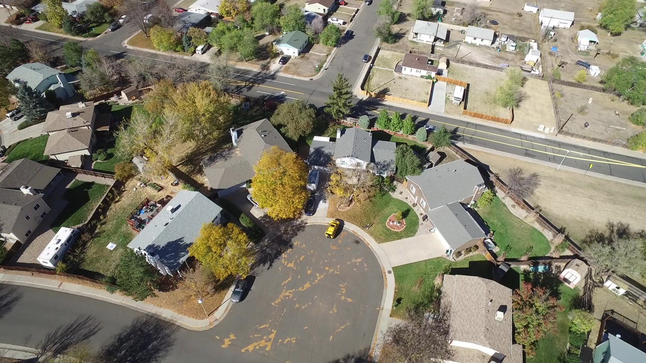 A high-angle aerial frame over Hidden Lake, Colorado shows detached homes, a curved cul-de-sac, lawns, dry lots, autumn trees, and no visible people.