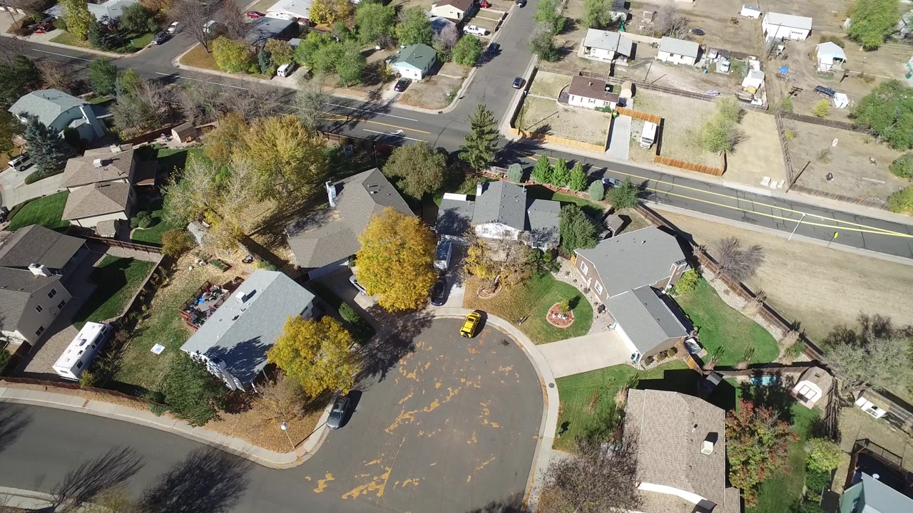 This Hidden Lake, Colorado aerial frame centers on gray-roofed houses beside a cul-de-sac, a yellow parked car, fenced yards, mature trees, and no visible people.