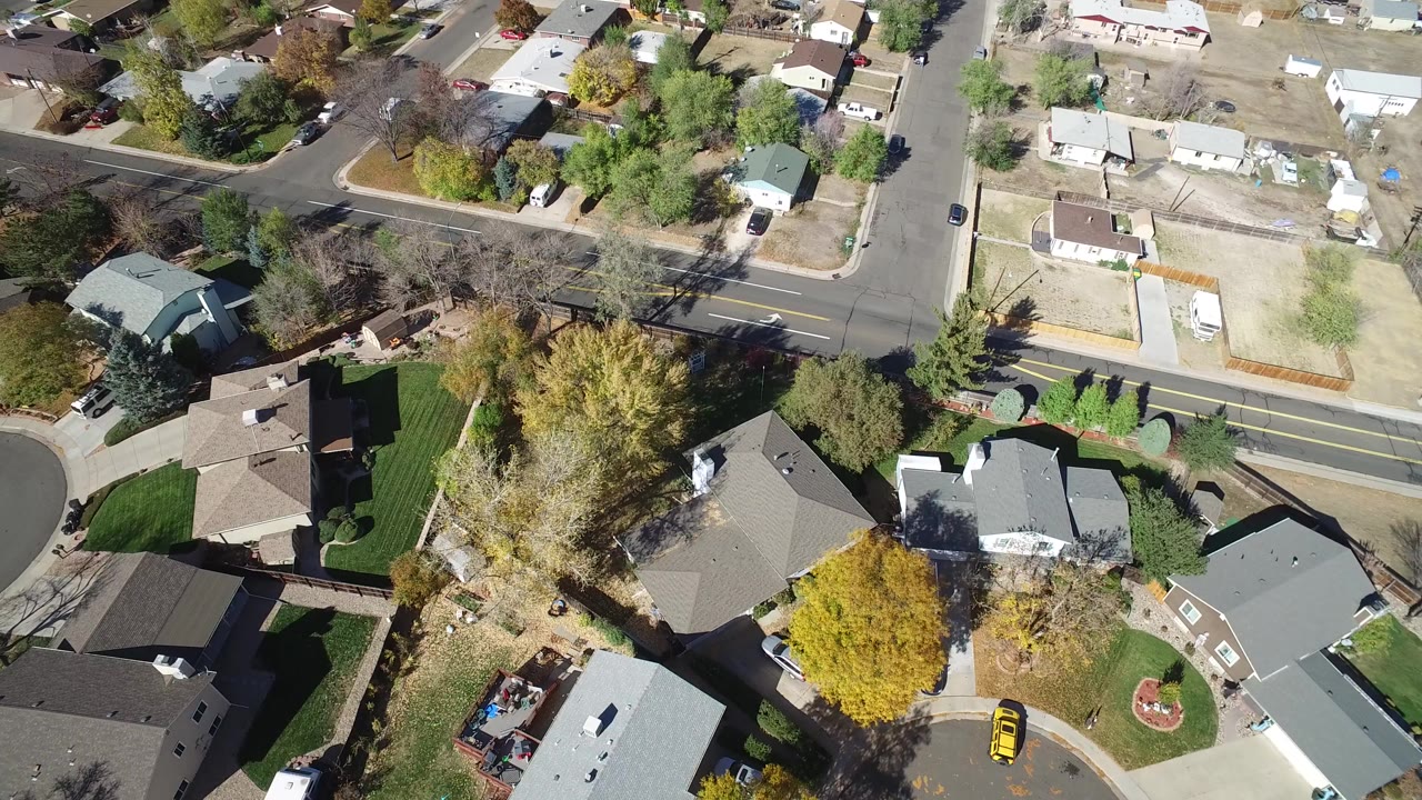 Overhead view of suburban homes, roads, lawns, and trees.