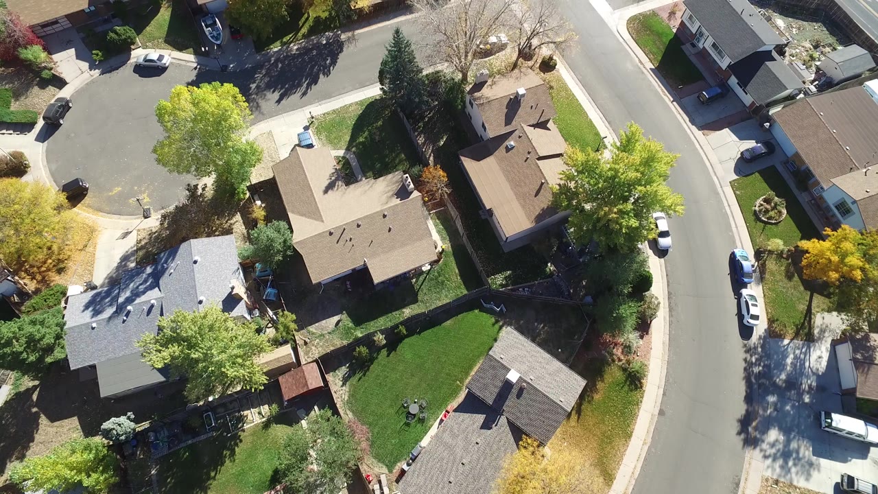 Second overhead frame in Hidden Lake, Colorado shows the same residential curve with tan and gray rooftops, driveways, parked vehicles, bright green trees, and no visible people.