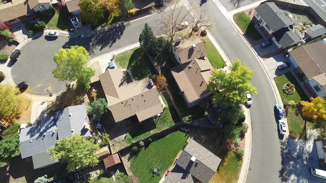 Top-down neighborhood view with rooftops, yards, trees, and a cul-de-sac edge.