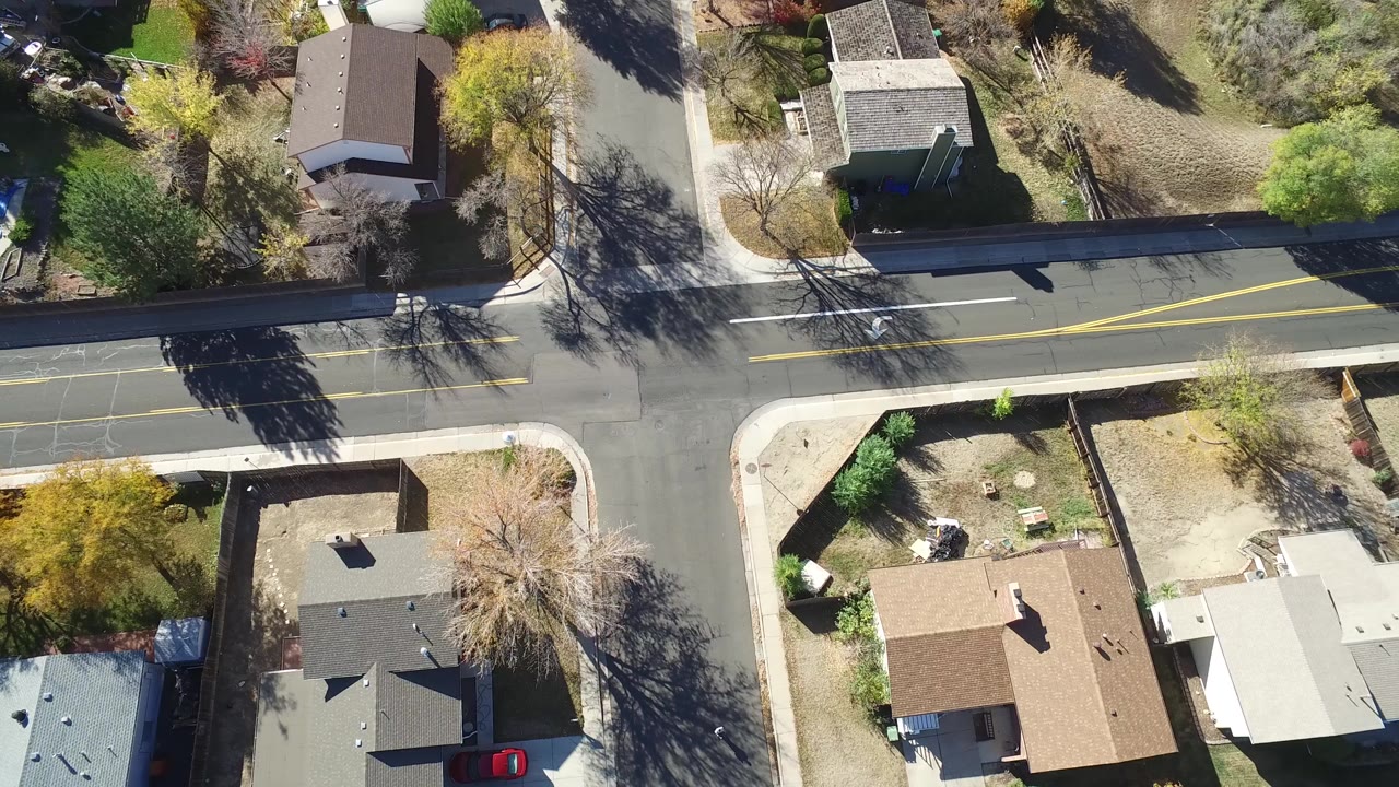 High overhead view in Hidden Lake, Colorado showing a residential intersection, detached houses, sidewalks, tree shadows, and no visible people.