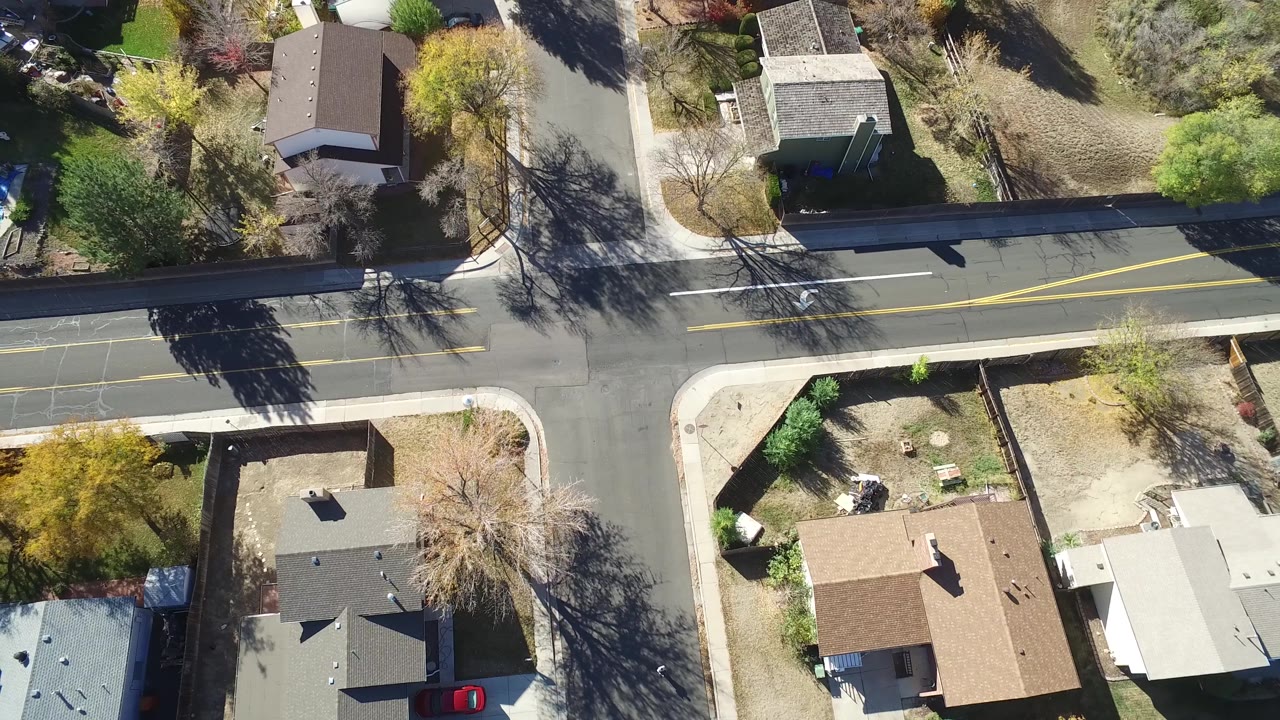 Aerial top view in Hidden Lake, Colorado with the main road across the frame, rooftops below it, bare trees, yellow foliage, and no visible people.
